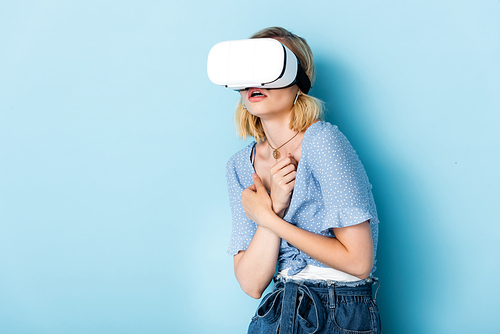 young and scared woman in virtual reality headset on blue