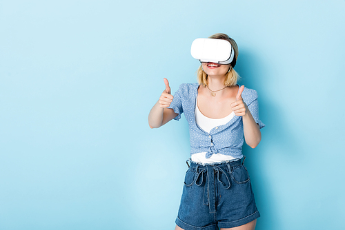 young woman in virtual reality headset showing thumbs up on blue