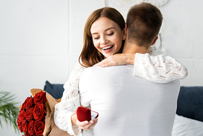 back view of of man with bouquet and smiling woman hugging him with box