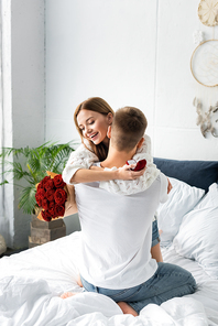 back view of of man with bouquet and smiling woman hugging him with box