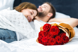 selective focus of bouquet and woman lying on smiling man on background