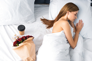 top view of woman sleeping in bed near paper cup and bouquet