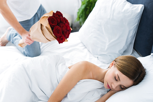 cropped view of man holding bouquet and woman sleeping in bed