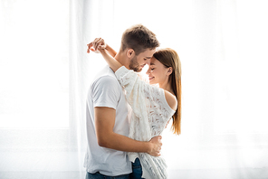 side view of handsome man hugging attractive and smiling woman in apartment