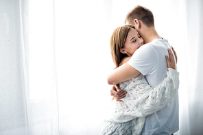 man hugging attractive and smiling woman in apartment