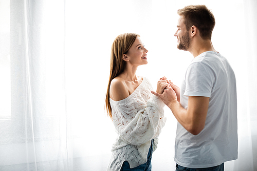 side view of handsome man holding hands with smiling woman in apartment
