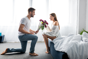 side view of handsome man giving bouquet to attractive woman in apartment