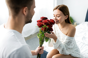 cropped view of man giving bouquet to attractive and smiling woman in apartment