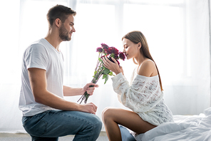 side view of handsome man giving bouquet to attractive woman in apartment