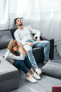 sad woman sitting on floor and handsome man sitting on sofa in robbed apartment