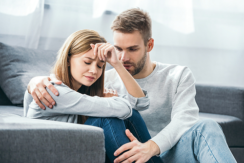 handsome man calming down sad woman in robbed apartment