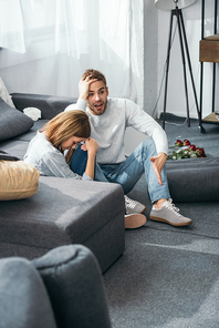 sad woman and shocked man sitting on floor in robbed apartment