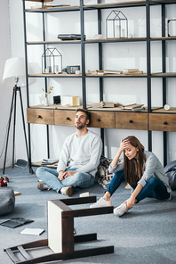 sad woman and handsome man sitting on floor in robbed apartment