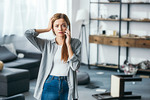 attractive and sad woman talking on smartphone in robbed apartment