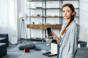 sad woman holding smartphone with blank screen in robbed apartment
