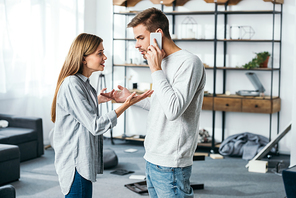 side view of angry woman and handsome man talking on smartphone in robbed apartment