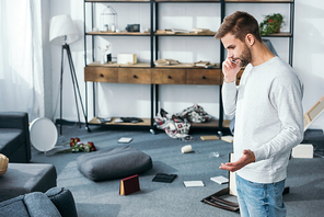 side view of handsome man talking on smartphone in robbed apartment