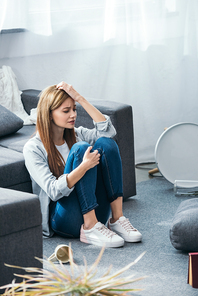 attractive and sad woman sitting on floor in robbed apartment