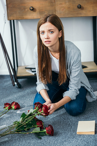 attractive and sad woman holding flowers in robbed apartment