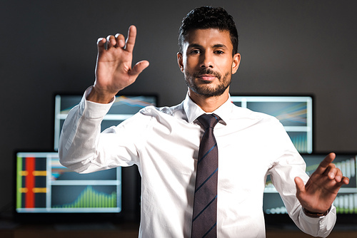 selective focus of bi-racial trader pointing with fingers and computers on background