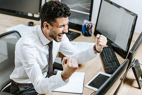 happy bi-racial trader showing yes gesture and looking at computer