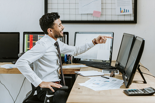 side view of smiling bi-racial trader pointing with finger at computer