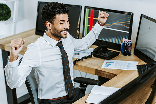 high angle view of smiling bi-racial trader looking at computer and showing yes gesture