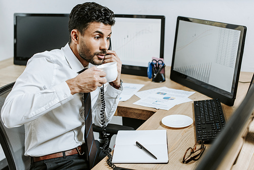 bi-racial trader talking on telephone and holding cup of coffee