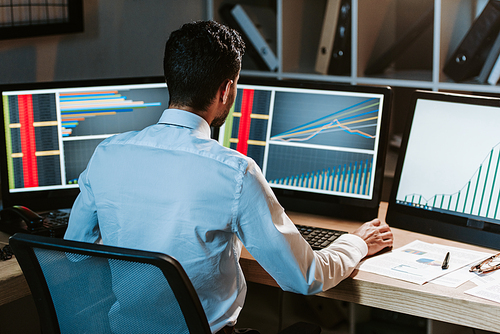 back view of bi-racial trader looking at computer with graphs