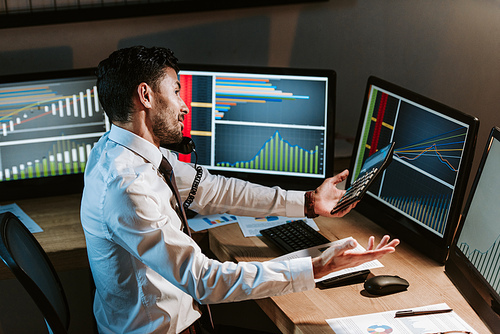 high angle view of bi-racial trader talking on telephone and looking at computer with graphs