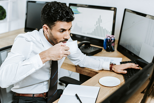 high angle view of bi-racial trader drinking coffee and looking at computer