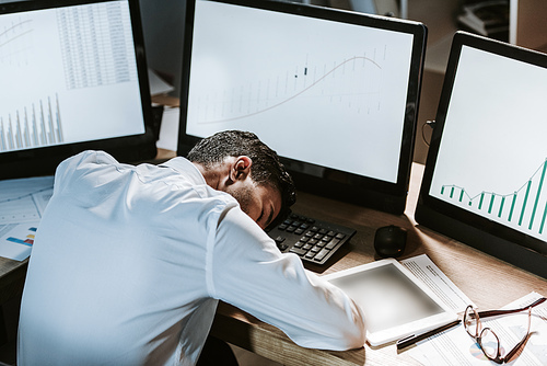 high angle view of bi-racial trader sleeping near computers with graphs