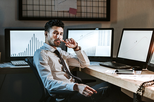 pensive bi-racial trader sitting near computers with graphs and