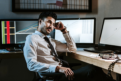 smiling bi-racial trader sitting near computers with graphs in office