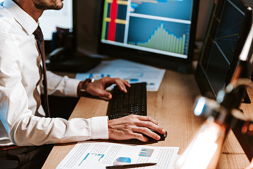 cropped view of bi-racial trader using computer and sitting at table