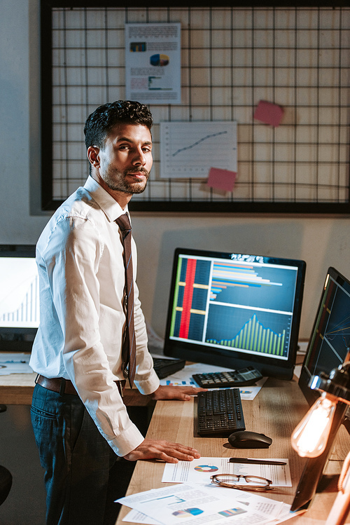 bi-racial trader standing near computers with graphs and 