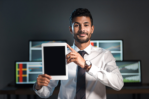 smiling bi-racial trader holding digital tablet and computers with graphs on background