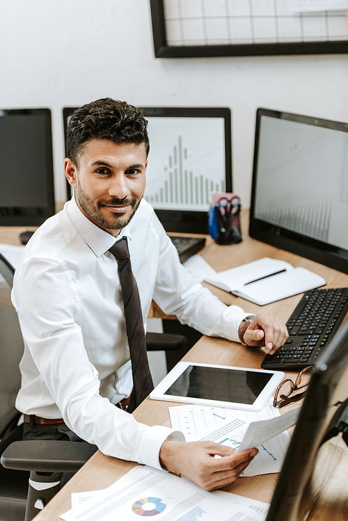 smiling bi-racial trader holding paper and sitting at table