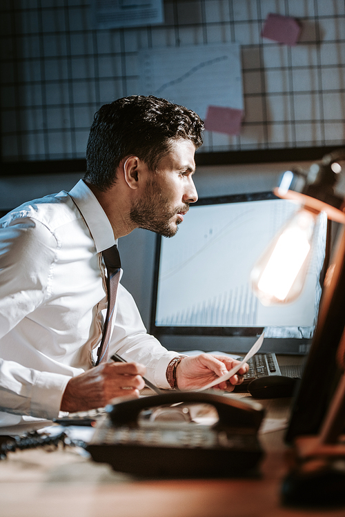 side view of handsome bi-racial trader using computer and sitting at table