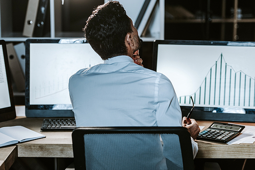 back view of bi-racial trader sitting near computers with graphs