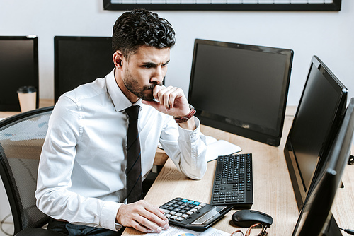 pensive bi-racial trader looking at computer and sitting at table