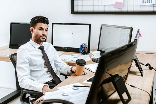 bi-racial trader looking at computer and holding paper cup