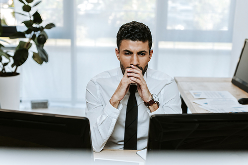 pensive and handsome bi-racial trader looking at computer in office