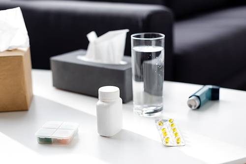 selective focus of glass of water near tissue box, inhaler and blister pack with pills