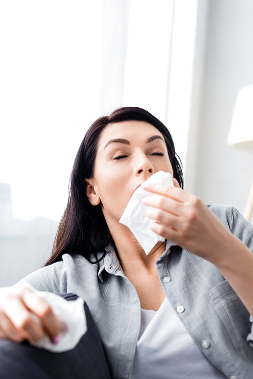 selective focus of allergic woman sneezing and holding napkins