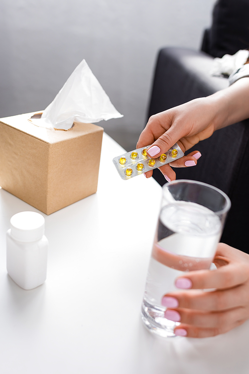 cropped view of allergic woman holding blister pack with pills and glass of water and tissue box