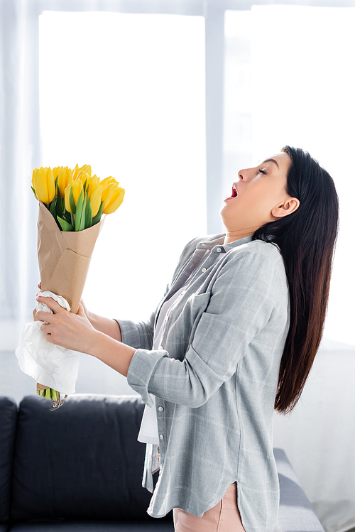 sneezing woman with pollen allergy and closed eyes holding tulips