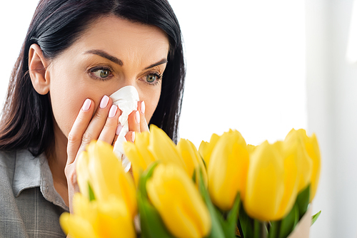 selective focus of woman with pollen allergy sneezing and looking at tulips