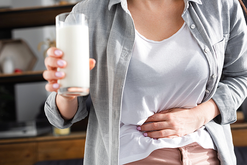 cropped view of woman with lactose intolerance holding glass of milk while touching stomach