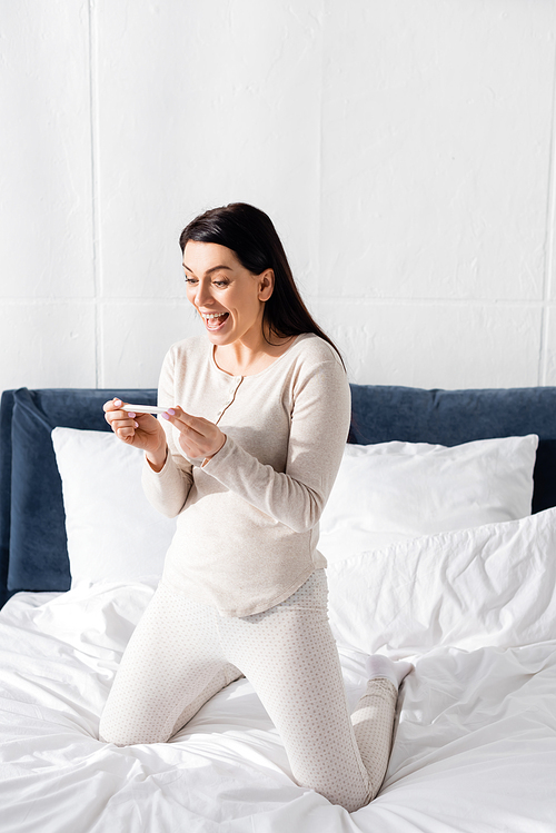 excited woman holding pregnancy test in bedroom